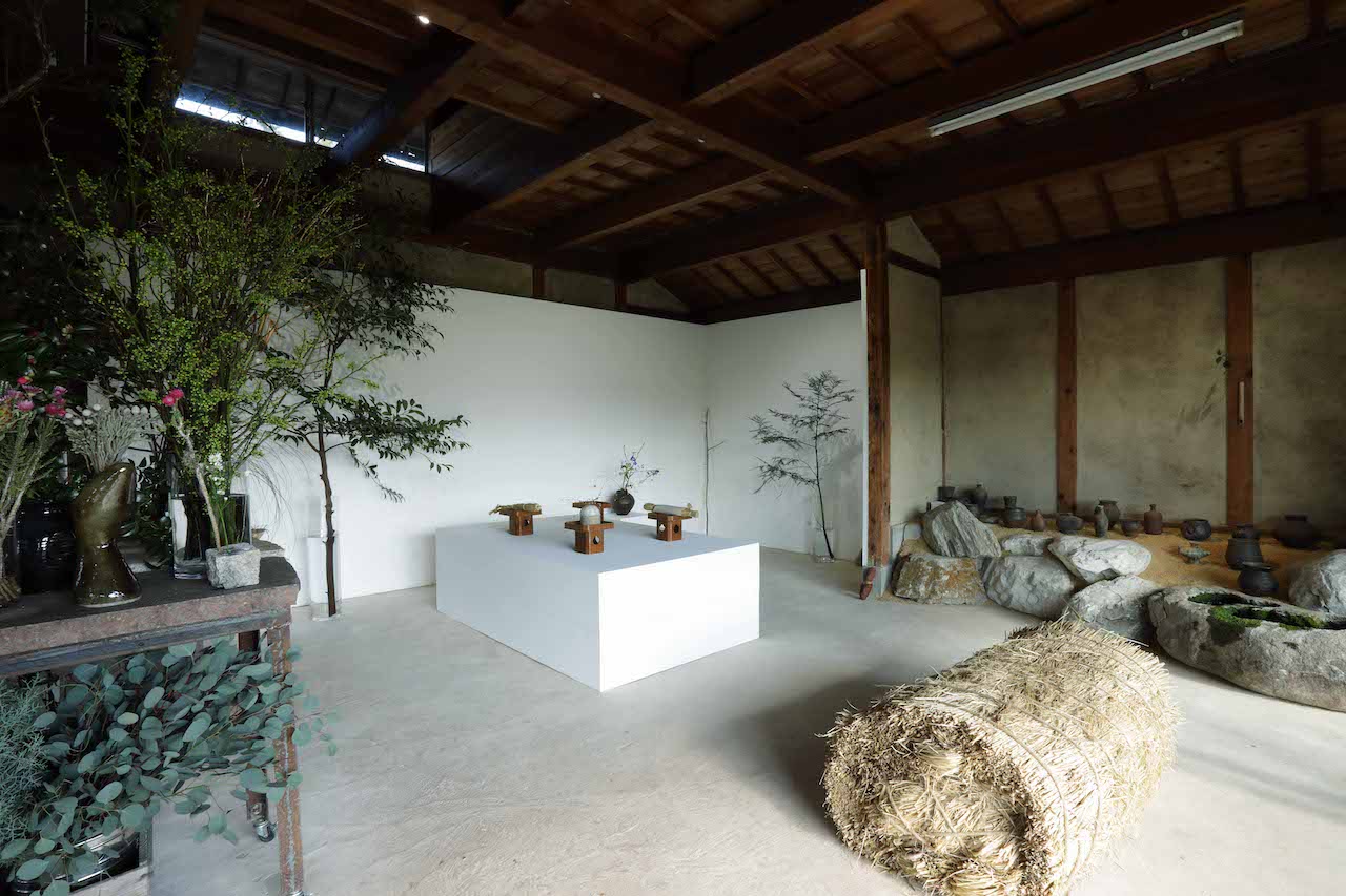 壁際に並んでいるのは日野町在住の陶芸作家・田中敬史さんと、aloでも使われていた山田洋次さんの花器たち。こちらはすべて購入可能。「棚を作って置いてみたら、しっくりきすぎて展示だと思われちゃって（笑）」。手前の巨大な藁の束は作品かと思いきや「椅子です、どうぞ座ってください」。
